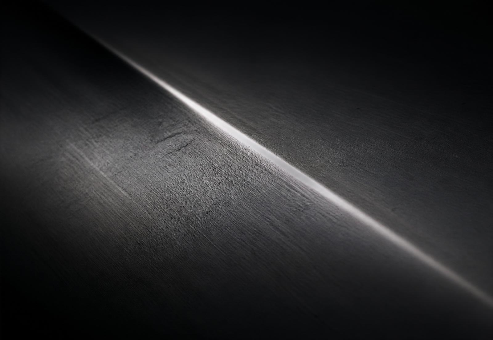 Macro detail of a brushed metal body panel crease catching a thin edge of light